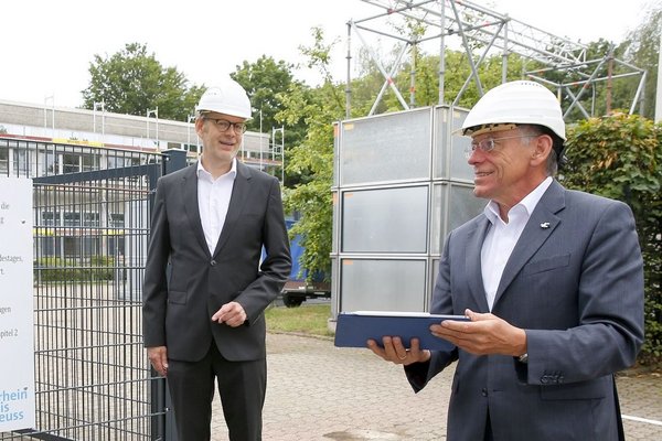 Schulleiter Markus Steinhauer, Projektleiter Franz Steves und Landrat Hans-Jürgen Petrauschke  mit Schutzhelmen stehen mit Abstand vor einem Baustellenschild