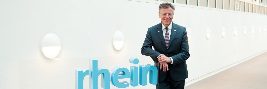 Landrat Hans-Jürgen Petrauschke lehnt an einem blauen 3-D-Logo des Rhein-Kreises Neuss