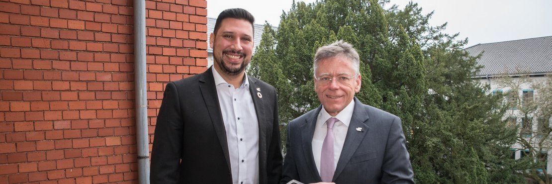 Landrat Hans-Jürgen Petrauschke und Thiago de Carvalho Zakrzewski stehen lächelnd auf einem Balkon. Landrat Petrauschke hält eine Trophäe in den Händen.