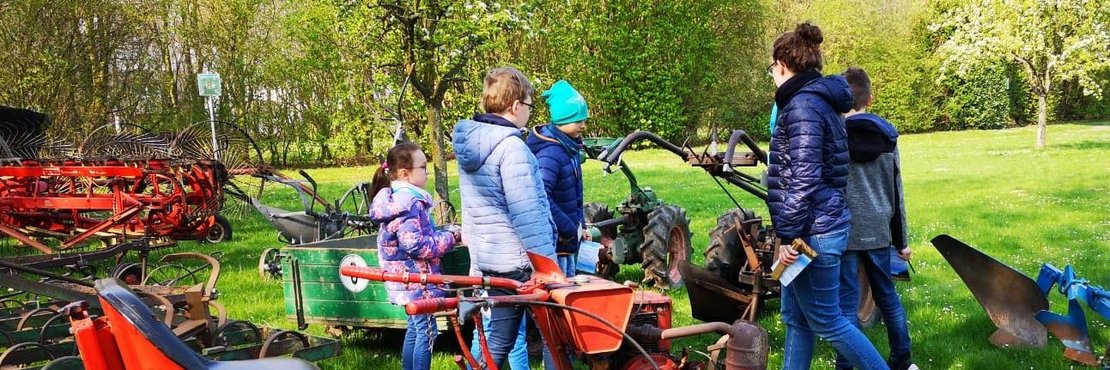 Kinder und Betreuerin schauen sich landwirtschaftliche Maschinen auf einer Wiese an