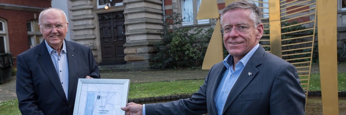 Landrat Petrauschke überreicht Kallen vor dem Ständehaus in Grevenbroich die Urkunde für den Sportehrenamtspreis des Rhein-Kreises Neuss