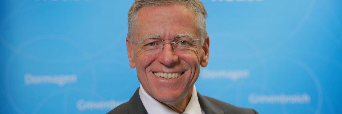 Landrat Hans-Jürgen Petrauschke lächelnd vor blauer Fotowand mit Logo Rhein-Kreis Neuss
