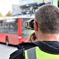 Das Bild zeigt von hinten einen Verkehrspolizisten, der mit einem Geschwindigkeitsmessgerät die Geschwindigkeit eines roten Busses misst. Der Bus ist im Hintergrund unscharf dargestellt, während der Polizist und sein Gerät im Vordergrund scharf abgebildet sind.  Der Polizist trägt eine dunkle Jacke und eine leuchtend gelbe Warnweste.  Das Display des Messgeräts zeigt eine Geschwindigkeit an. © Polizei Rhein-Kreis Neuss