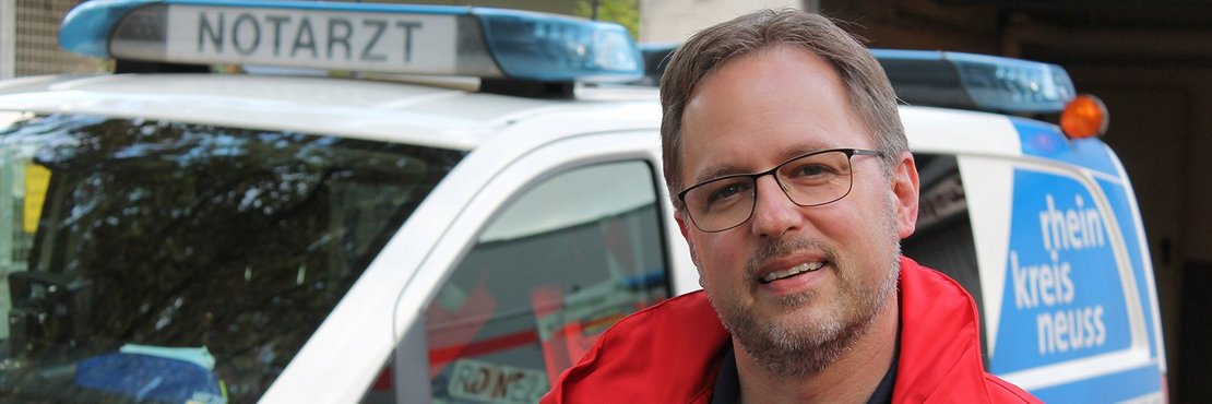 Marc Zellerhoff in Rettungsdienstjacke vor Notarztwagen des Rhein-Kreises Neuss