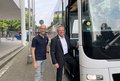Zwei männliche Personen stehen an der Eingangstüre eines weißen Reisebusses und lächeln.