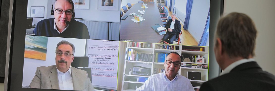 Eine Person sitzt vor einem Bildschirm im Rahmen einer Telefonkonferenz