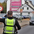 Das Bild zeigt einen deutschen Polizisten von hinten, der mit erhobenem Arm ein rotes „Halt Polizei“-Schild hält und einen vorbeifahrenden PKW anhält.  Im Hintergrund ist ein Autohaus mit mehreren parkenden Autos zu sehen. © Polizei Rhein-Kreis Neuss