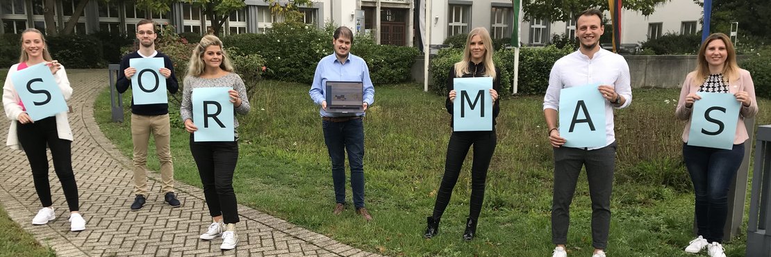 Die genannten Personen stehen mit Abständen vor dem Kreishaus Grevenbroich. Sie halten Schilder in der Hand mit den Buchstaben des Wortes SORMAS. Schellhorn hält ein Notebook.