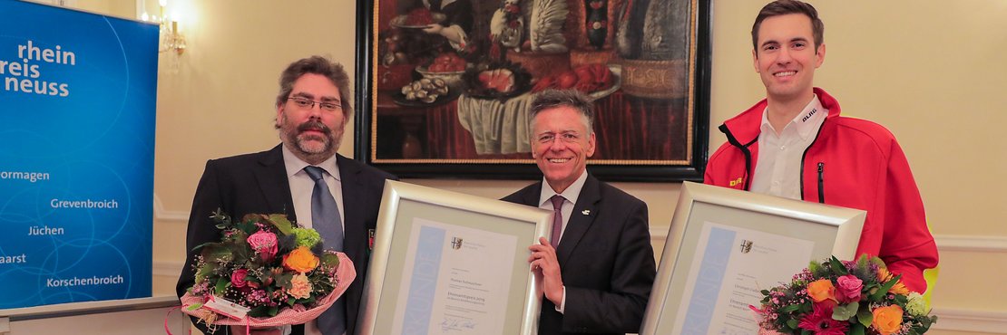 Landrat Hans-Jürgen Petrauschke, Thomas Tscheuschner und Christoph Claßen mit Blumensträußen und Urkunden in den Händen