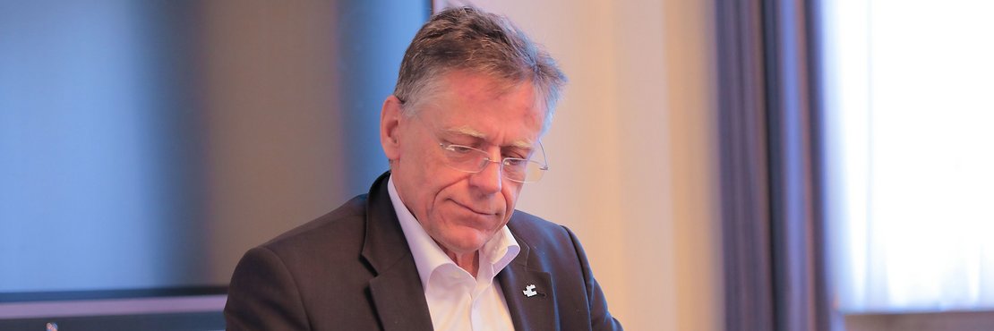 Landrat Hans-Jürgen Petrauschke mit Mobiltelefon und Schreibblock am Schreibtisch