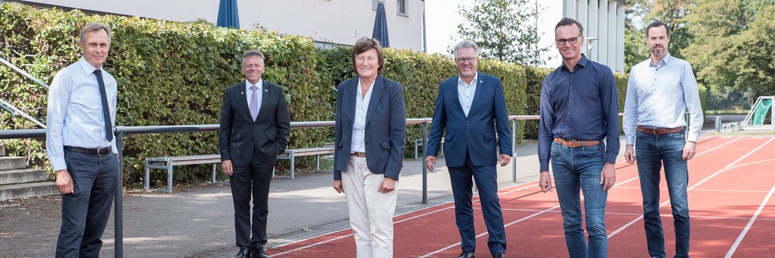 Johannes Gillrath, Landrat Hans-Jürgen Petrauschke, Dieter Welsink, Dirk Schröter, Henning Heinrichs und Uschi Schmitz stehen mit Abstand von circa 2 Metern zueinander auf einer Tartanbahn.