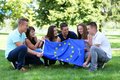Eine Gruppe junger Menschen sitzt auf einer Wiese und hält gemeinsam eine Europafahne 