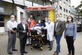 Landrat Hans-Jürgen Petrauschke steht mit einigen Menschen (siehe Bildbeschreibung) au der Rückseite eines neuen Rettungswagens. Alle tragen einen Mund-Nasenschutz. 