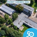 Das Bild zeigt eine Luftaufnahme der Herbert-Karrenberg-Schule. Man sieht mehrere Gebäudeteile, die teilweise modern und teilweise älter aussehen, sowie einen begrünten Außenbereich. Im Vordergrund befindet sich ein Logo zum 50-jährigen Jubiläum des Rhein-Kreises Neuss. © Rhein-Kreis Neuss