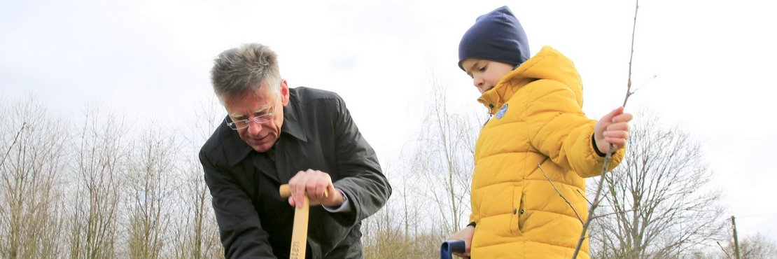 Landrat Hans-Jürgen Petrauschke und ein Kind pflanzen einen Baum