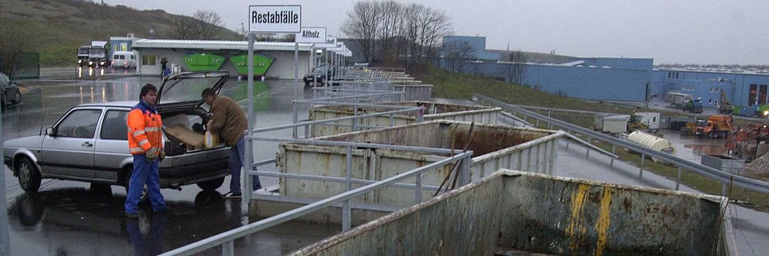 Zwei männliche Personen werfen Restabfälle in einen Container auf einer Deponie