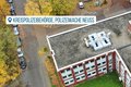Das Bild zeigt eine Luftaufnahme der Kreispolizeibehörde, Polizeiwache Neuss.  Im Vordergrund ist ein Teil des Gebäudes mit dem Dach zu sehen, auf dem sich diverse technische Anlagen befinden.  Im Hintergrund sind Parkplätze mit Autos und die umliegende herbstliche Landschaft mit gelb-braunen Bäumen sichtbar. Rechts unten im Bild befindet sich ein blaues Logo, das auf das 50-jährige Jubiläum des Rhein-Kreises Neuss hinweist.