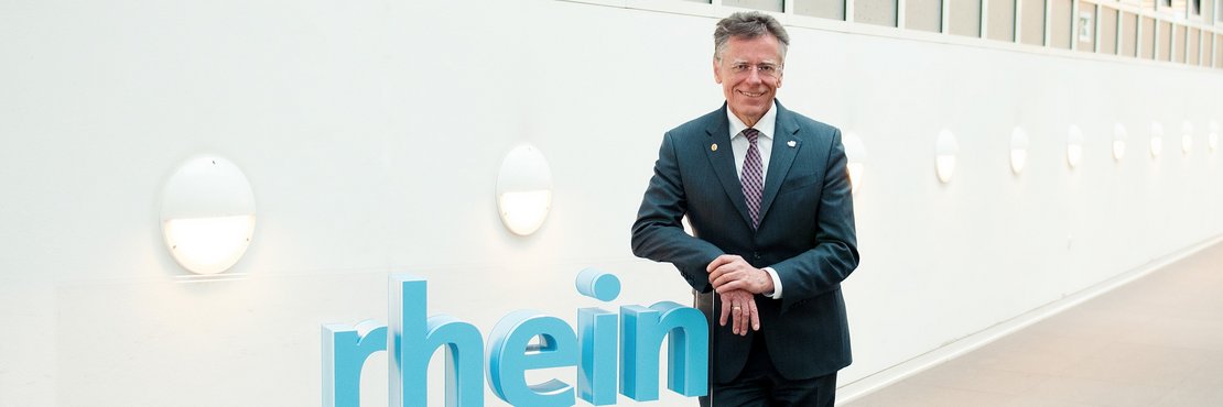 Landrat Hans-Jürgen Petrauschke lehnt an einem blauen 3-D-Logo des Rhein-Kreises Neuss