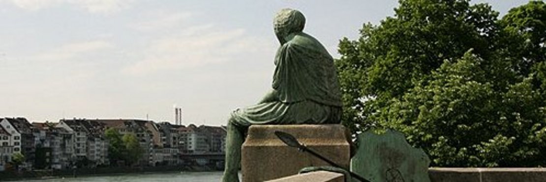 Denkmal: Statue sitzt auf einer Mauer an einem Fluss