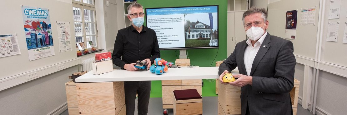 Landrat Petrauschke und Heling (beide mit Mund-Nasen-Schutz) stehen im modernen Schulungsraum des Medienzentrums und halten Lernspielzeug in Ihren Händen.