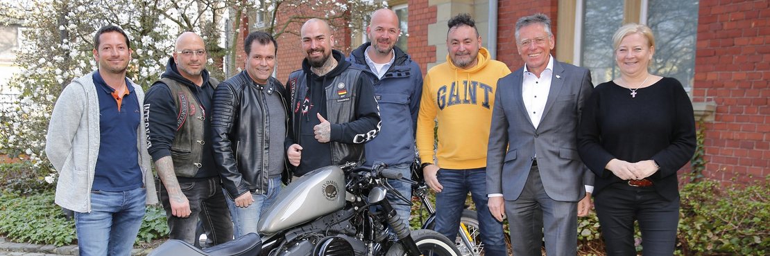 Gruppenfoto. Menschen stehen hinter einem Motorrad. 