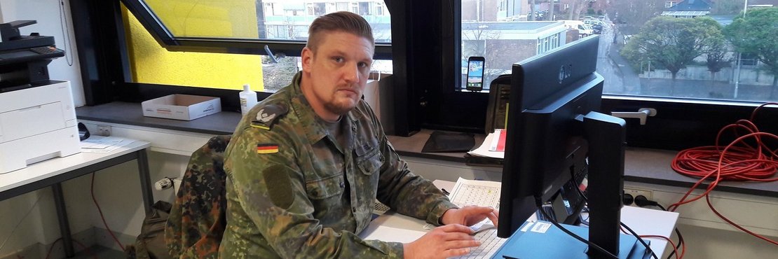 Soldat in Bundeswehr-Uniform sitzt am Schreibtisch vor Computer. 