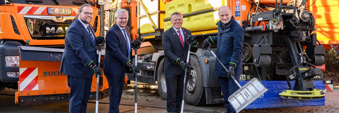 Gruppenfoto mit Schneeschaufeln vor Winterdienst-Fahrzeugen