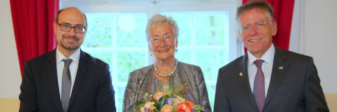 Landrat Hans-Jürgen Petrauschke (r.) mit Urkundenmappe in den Händen steht neben Ingrid Landen mit Blumenstrauß sowie dem Stellvertretenden Bürgermeisters Sven Schümann aus Neuss.