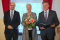 Landrat Hans-Jürgen Petrauschke (r.) mit Urkundenmappe in den Händen steht neben Ingrid Landen mit Blumenstrauß sowie dem Stellvertretenden Bürgermeisters Sven Schümann aus Neuss.