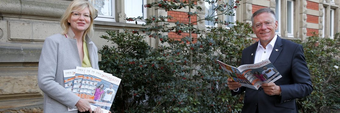 Landrat Petrauschke und Frau Trampen stehen mit Abstand vor einem Gebäude. Sie hält Broschüren in der Hand, er hat eine Broschüre aufgeschlagen.