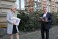 Landrat Petrauschke und Frau Trampen stehen mit Abstand vor einem Gebäude. Sie hält Broschüren in der Hand, er hat eine Broschüre aufgeschlagen.