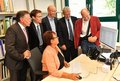 Personengruppe rund um einen Schreibtisch. Alle schauen auf einen Bildschirm.