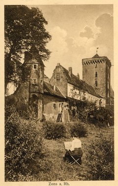 Eine alte Postkarte. Sie zeigt eine Frau, die in den Rheinwiesen sitzend die Feste Zons zeichnet