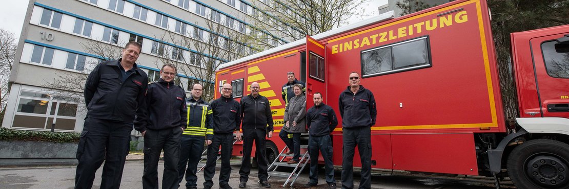 uniformierte und ziviel gekleidete Mitarbeitende der Kreisleitstelle vor dem Einsatzleitwagen-2, der vor dem Kreishochhaus in Grevenbroich steht