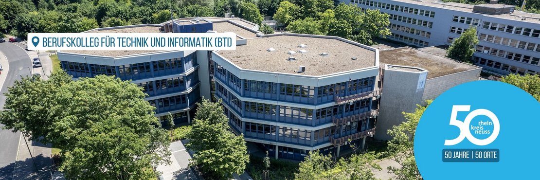 Das Bild zeigt eine Luftaufnahme des Berufskollegs für Technik und Informatik (BTI) im Rhein-Kreis Neuss.  Das Gebäude ist ein mehrstöckiger, sechseckiger Bau, umgeben von Bäumen und anderen Gebäuden. Im Bild ist auch ein Logo zu sehen, das auf das 50-jährige Jubiläum des Rhein-Kreises Neuss hinweist.