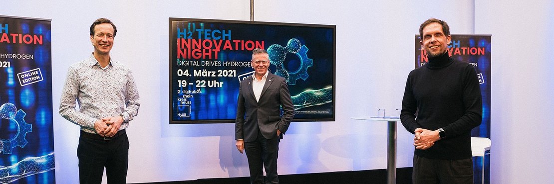 In der Bildbeschreibung genannte Herren stehen mit Abständen vor einem Monitor mit der Information: H2 Tech Innovation Night, 04. März 2021, 19-22 Uhr