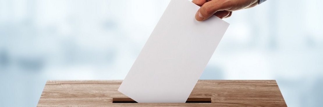Eine Hand wirft einen Brief in eine Wahlurne. (dekorativ)