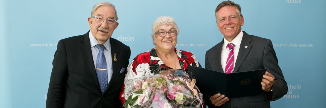 Zwei männliche Personen und weibliche Person in der Mitte mit einem Blumenstrauß