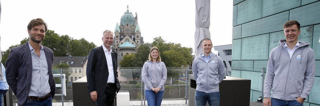 Kreisdirektor Dirk Brügge und die Sichtungstrainer Lars Bohnert, Stefanie Schiffer, Patrik Lamm und Tom Möller stehen mit Abstand zueinander auf der Dacherrasse der Pegelbar in Neuss. Im Hintergrund ist das Quirinusmünster zu sehen. 