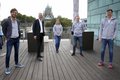 Kreisdirektor Dirk Brügge und die Sichtungstrainer Lars Bohnert, Stefanie Schiffer, Patrik Lamm und Tom Möller stehen mit Abstand zueinander auf der Dacherrasse der Pegelbar in Neuss. Im Hintergrund ist das Quirinusmünster zu sehen. 