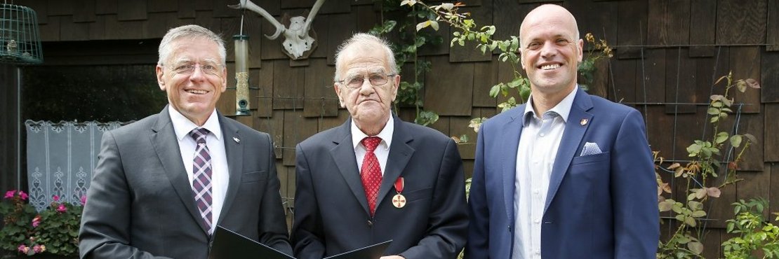 Landrat Hans-Jürgen Petrauschke und Bürgermeister Klaus Krützen stehen mit Hans-Dieter von Montfort draußen vor einem Haus. Hans-Dieter von Montfort trägt die Bundesverdienstmedaille