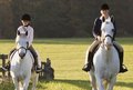 Zwei Personen auf Pferden reiten über eine Wiese