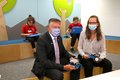 Landrat Hans-Jürgen Petrauschke und Bentje Lefers bei der Eröffnung der HABA Digitalwerkstatt Rhein-Kreis Neuss. Beide sitzen auf einer Bank und tragen einen Mund-Nasenschutz. 