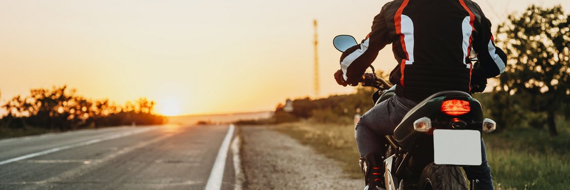 Person auf einem Motorrad steht am Seitenstreifen einer unbefahrenen Straße