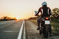 Person auf einem Motorrad steht am Seitenstreifen einer unbefahrenen Straße