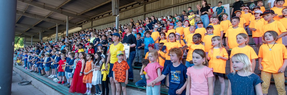 Viele Kinder stehen auf einer Tribüne. 