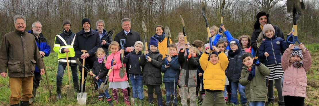 Landrat Hans-Jürgen Petrauschke mit einer Gruppe Grundschulkinder und Lehrern, die Spaten in die Höhe halten.