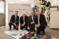 Vier männliche Personen kniend vor einem Technikbausatz