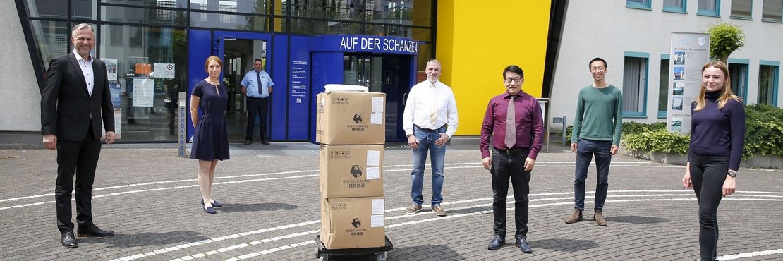Kreisdirektor Dirk Brügge mit Julia Beusch, Oliver Klein, vor ihnen stehen mehrere Kartons mit Schutzanzügen