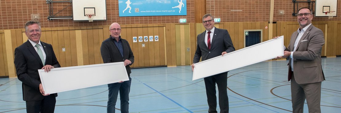 Landrat Hans-Jürgen Petrauschke, Michael Schlesiger, Edelbert Jansen und Harald Vieten halten zwei LED-Paneele in einer Sporthalle